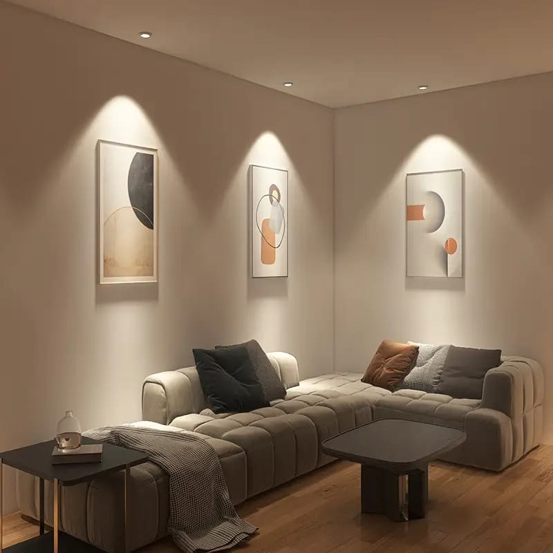 A living room in the evening: three deep anti-glare downlights wash soft light over framed wall art above a sofa