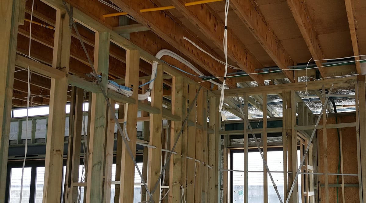 Cables run through a timber wall frame and along the ceiling joists of a home under renovation, before the walls are lined