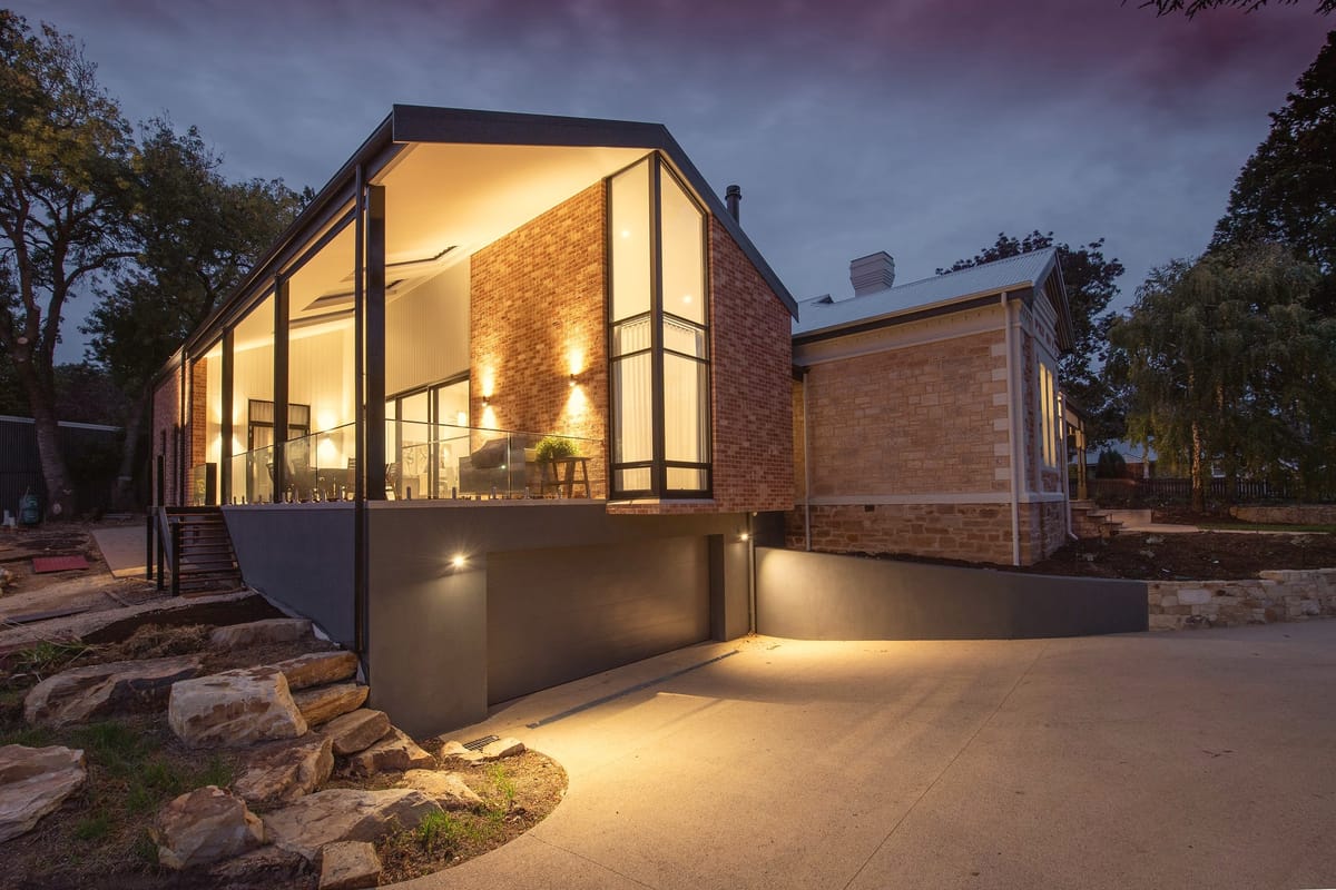 A modern home at dusk, warm light inside and garden steps lit outside