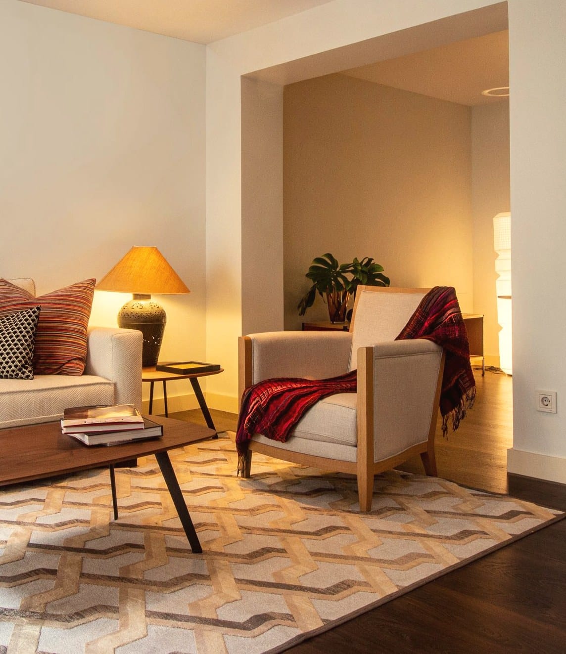 A living room corner in the evening, lit by a warm table lamp, with soft light on the walls