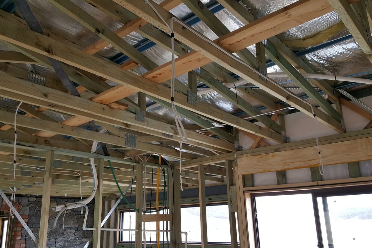 New cables run through the timber ceiling frame of a home at rough-in, before the ceiling is lined