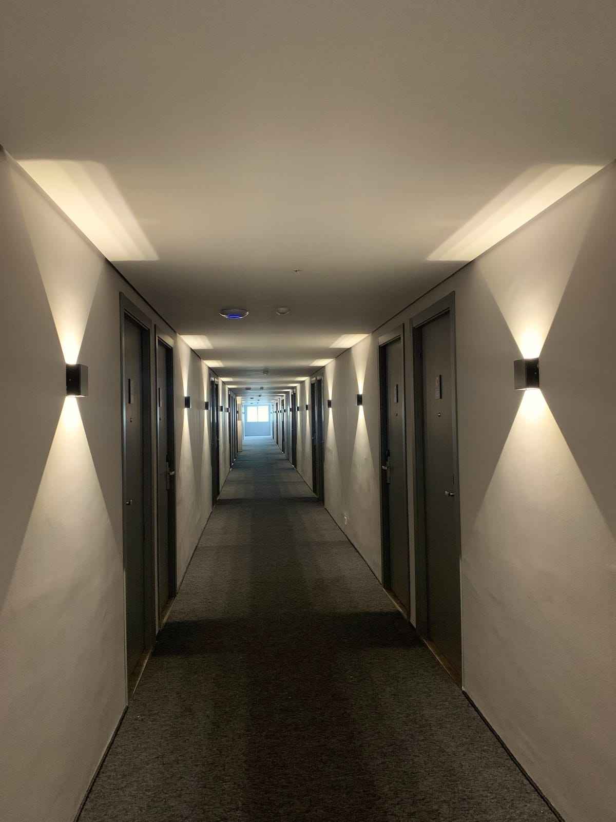 A long building corridor with every wall light on and nobody in it