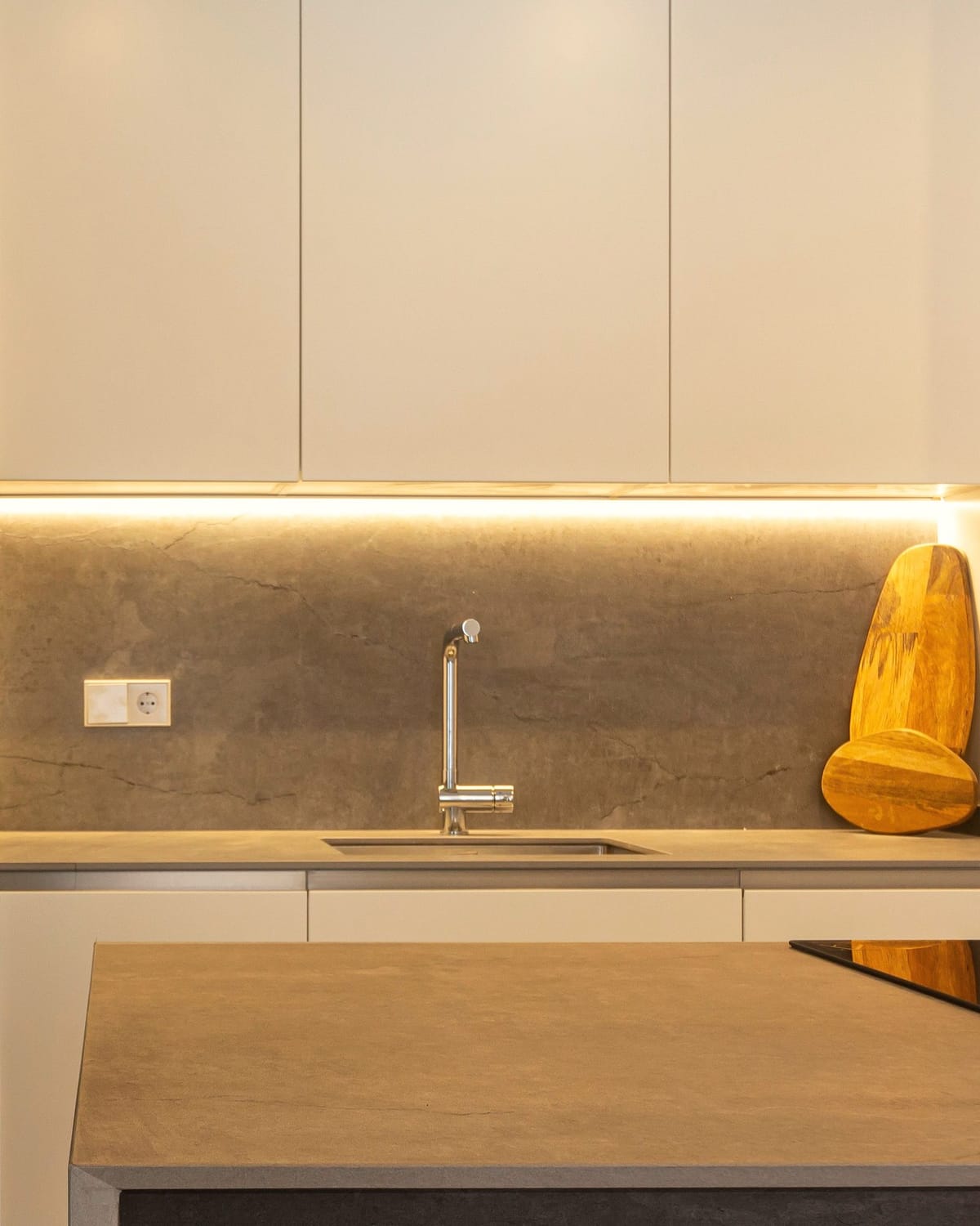 Kitchen cabinets with a smooth, continuous LED strip lighting the stone splashback below