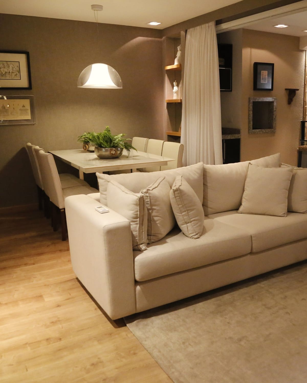 A lived in living and dining room in the evening, lit by ceiling downlights and a pendant over the table