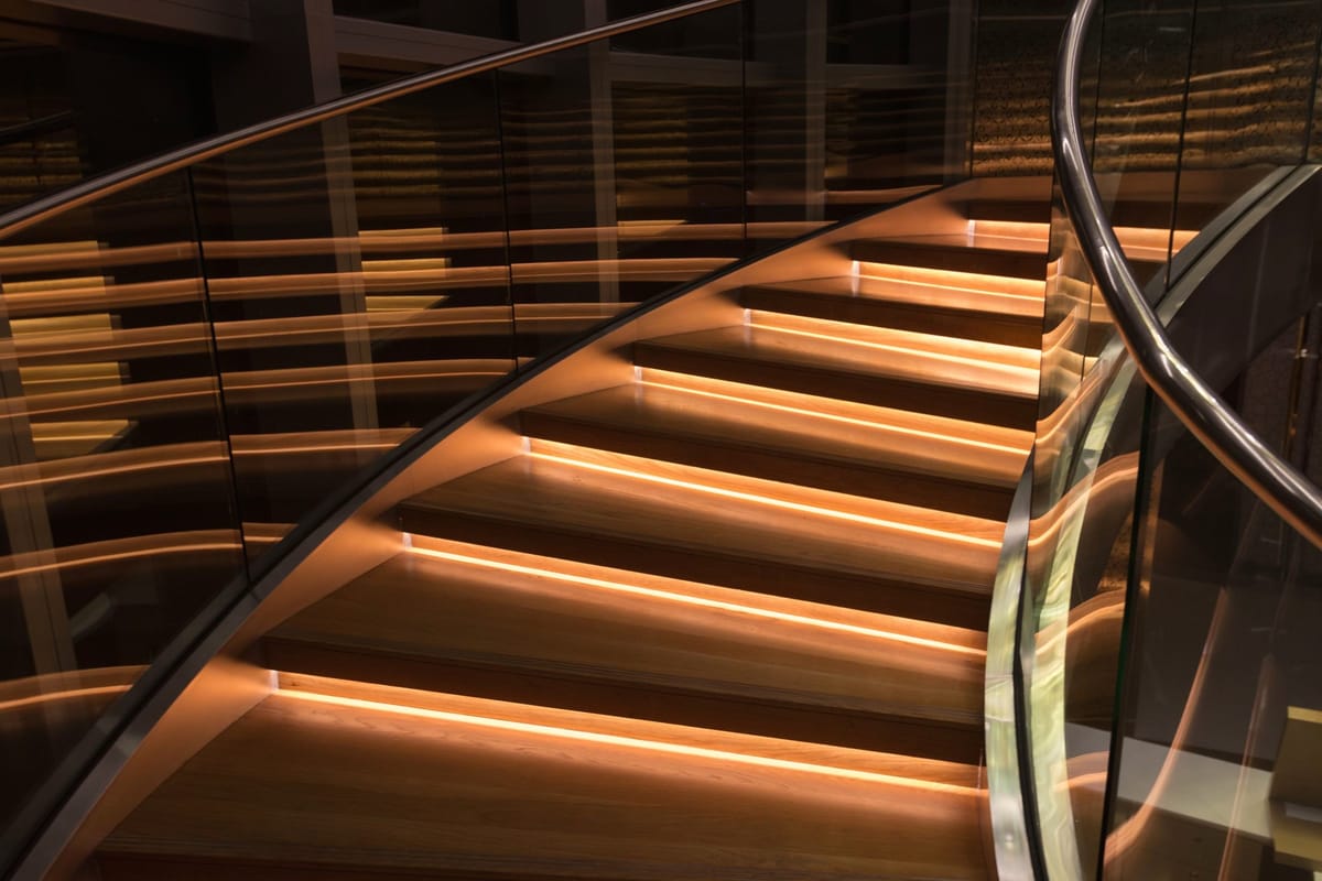 A curved timber staircase at night, each step lit by a warm concealed LED strip