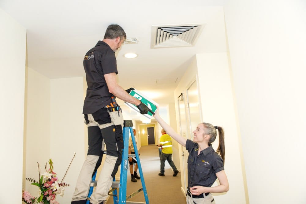 Two LED Solutions electricians working on corridor lighting, one on a ladder