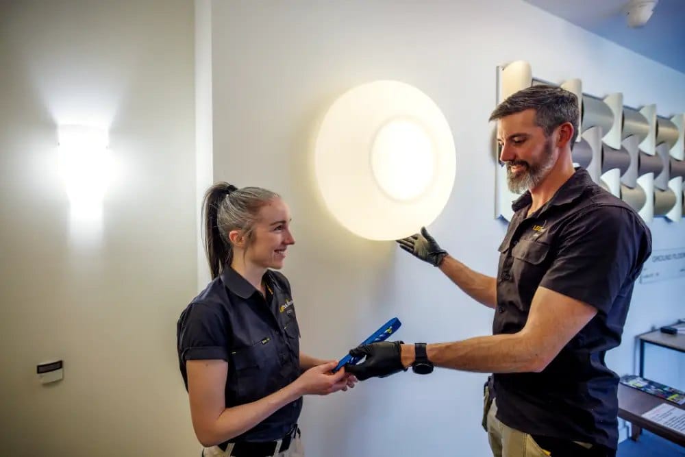 Kieran and a team member from LED Solutions fitting a large wall light in a building corridor